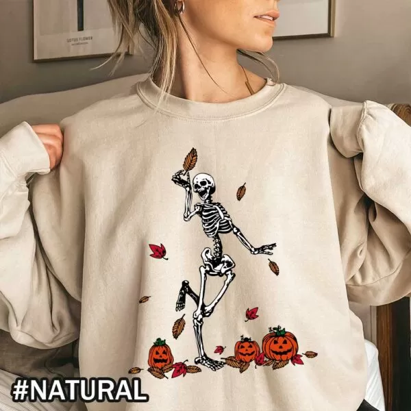 A happy skeleton holding a fall tree leaf and dancing around Jack-o-lantern carved pumpkins on a vintage Halloween sweatshirt